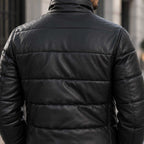 A close-up back view of a man wearing a black quilted leather jacket in an outdoor urban setting.