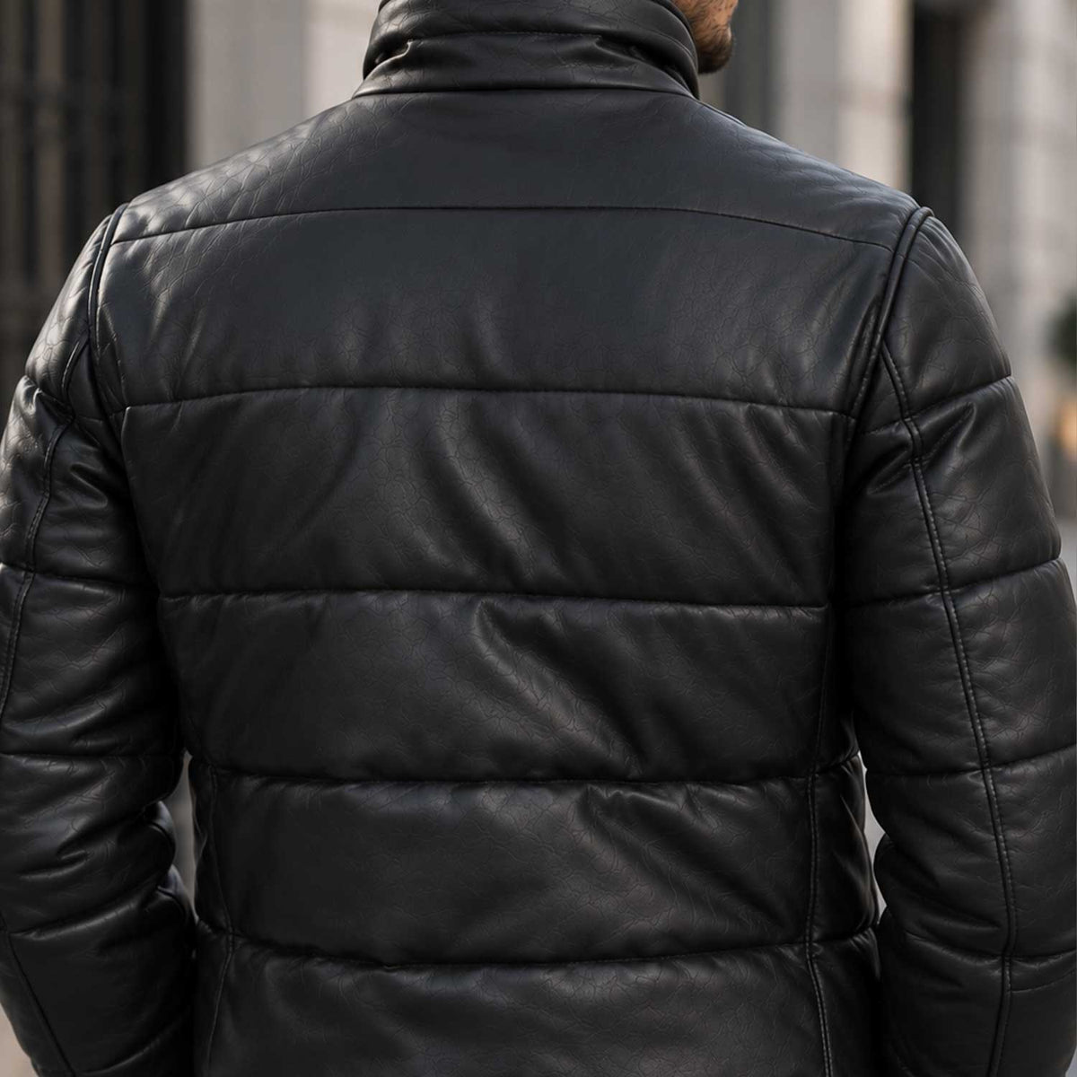 A close-up back view of a man wearing a black quilted leather jacket in an outdoor urban setting.