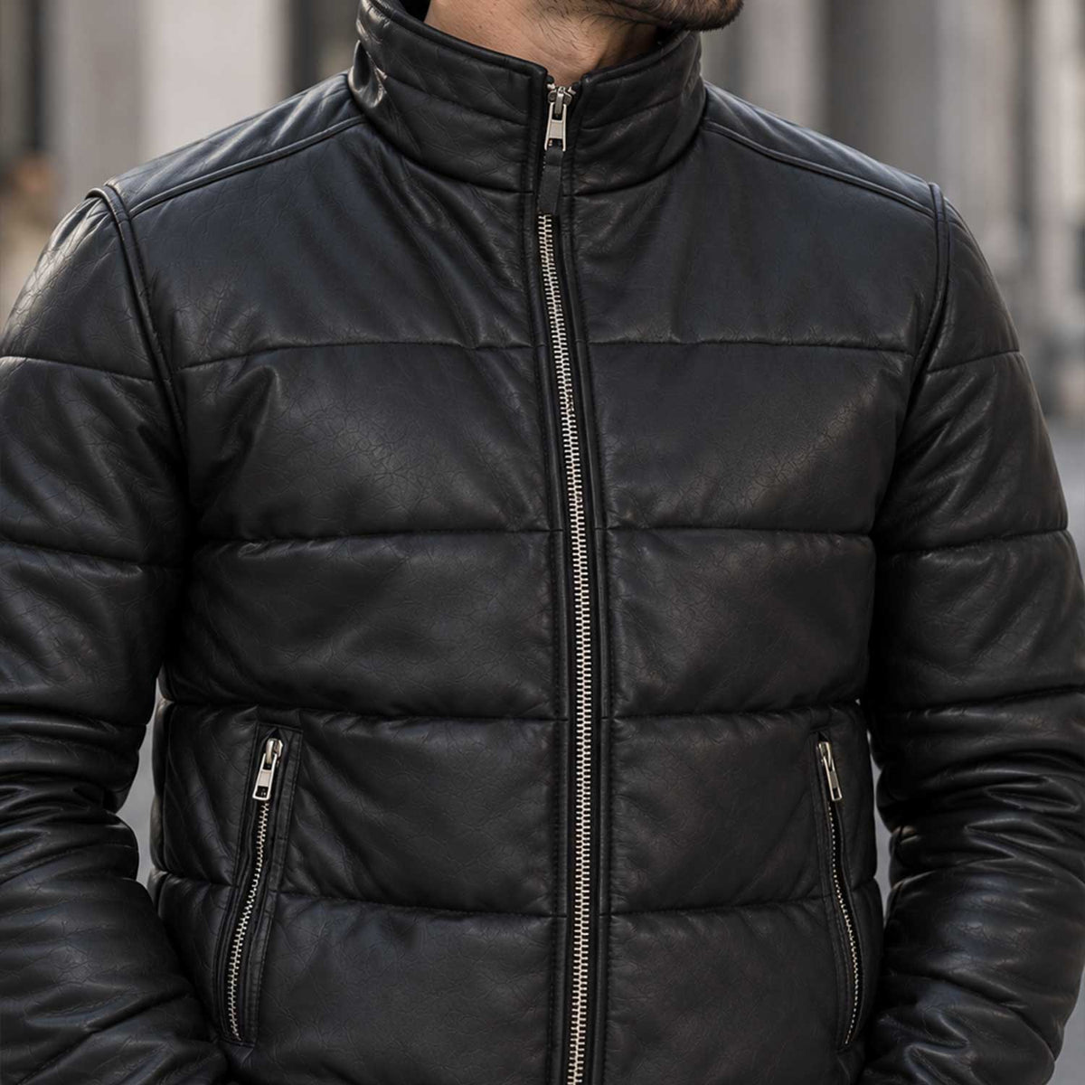 A close-up of a man wearing a black quilted leather jacket with a stand-up collar, front zipper, and zippered hand pockets.